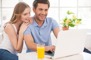 Surfing the net together. Cheerful young couple surfing the net together while sitting close to each other and looking at the laptop photo