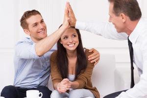 tenemos un trato. un joven feliz aplaudiendo con un agente financiero mientras se sienta junto a su esposa foto