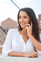 Good news from friend. Beautiful young woman talking on the mobile phone and smiling while standing outdoors photo