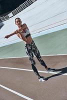 Her body is perfect. Full length of young woman in sports clothing stretching while exercising outdoors photo