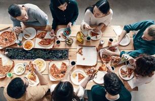Time for pizza. Top view of young people in casual wear picking pizza while having a dinner party indoors photo
