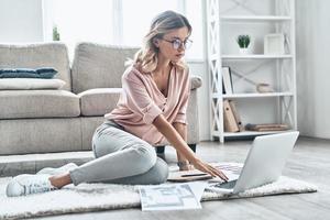 joven y lleno de ideas. una joven pensativa con anteojos que trabaja usando una computadora mientras está en el suelo en casa foto