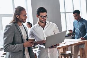 Discussing risky ideas. Two young modern men in smart casual wear using laptop while working time in the creative office photo