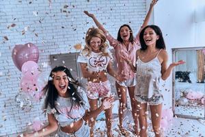 Yeah Four attractive young women in pajamas smiling and gesturing while jumping in the bedroom with confetti flying everywhere photo