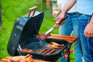 Barbecuing meat to perfection. Close-up of two people barbecuing meat on the grill while standing outdoors photo