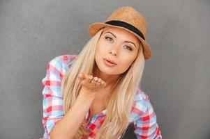 Kiss for you. Flirty young woman blowing kiss and looking at camera while standing against grey background photo