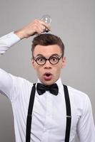 Fresh idea Surprised young man in bow tie and suspenders holding light bulb upon his head while standing against grey background photo