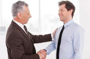 Business partners. Two cheerful business men shaking hands and looking at each other photo