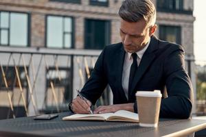 Confident mature businessman making notes while sitting on business center terrace photo