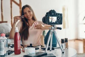 Good looking young woman applying lip gloss and smiling while making social media video photo