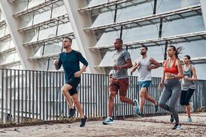 toda la longitud de los jóvenes en ropa deportiva trotando mientras hacen ejercicio al aire libre foto