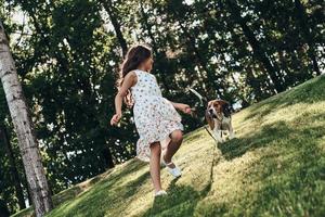 Full length of cute little girl playing with her dog while running outdoors photo