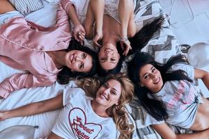 bellezas alegres. vista superior de cuatro mujeres jóvenes atractivas sonriendo mientras están acostadas en la cama en casa foto