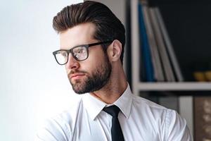 Confident and handsome. Portrait of handsome young businessman in glasses looking away while standing in office photo