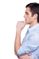 Thinking about solution. Side view of thoughtful young man in blue shirt holding hand on chin and looking away while standing isolated on white photo