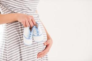 esperando un niño. vista lateral imagen recortada de una mujer embarazada sosteniendo pequeños zapatos cerca del abdomen foto