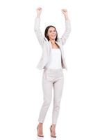 Happy businesswoman. Full length of happy young businesswoman in suit keeping arms raised and smiling while standing against white background photo