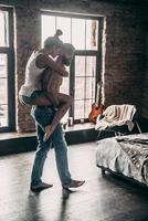 Perfect match.  Beautiful young couple enjoying free time at home while shirtless man carrying attractive woman on shoulders photo