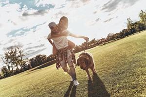 Simply happy. Full length of handsome young man carrying young attractive woman on shoulders while walking with their dog outdoors photo