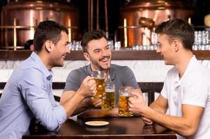 pasar tiempo en el bar. tres alegres amigos bebiendo cerveza en el bar foto