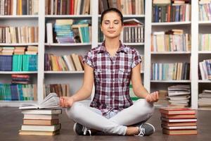 Time to chill. Beautiful young woman keeping her eyes closed and meditating while sitting at the library photo
