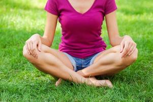 Relaxing in nature. Close-up of woman sitting in lotus position in green grass photo