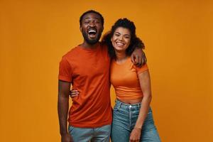 hermosa joven pareja africana mirando a la cámara y sonriendo mientras está de pie contra el fondo amarillo foto