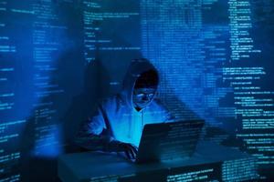 Concentrated young man in hooded shirt using computer against dark background photo