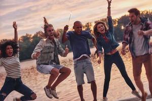 Enjoying the moment. Group of young people in casual wear smiling and gesturing while jumping on the pier photo