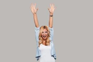 I did it Happy young woman keeping hands raised and looking at camera while standing against grey background photo