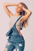 Born to be free. Studio shot of beautiful young woman in jeans overall holding hands in hair and keeping eyes closed photo