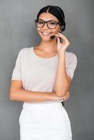 Always ready to help you. Smiling young female customer service looking at camera while standing against grey background photo