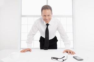 Architect at work. Cheerful senior man in shirt and tie leaning at the table with a blueprint laying on it photo