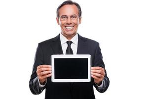 Your message on his tablet. Confident mature man in formalwear and glasses showing monitor of his digital tablet and smiling while standing isolated on white background photo