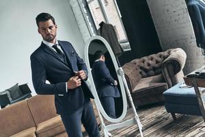 Used to look perfect. Handsome young man in full suit looking away and adjusting his jacket while standing indoors photo