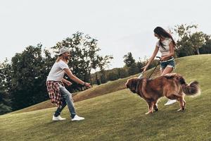 Real fun.  Full length of beautiful young couple playing with their dog while spending time outdoors photo