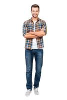 Reliable guy. Full length of smiling young man keeping arms crossed and looking at camera while standing against white background photo