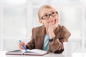 Daydreamer. Thoughtful little girl in glasses and formalwear sitting at the table and holding hand photo