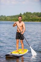 hombre en paddleboard. apuesto joven surfeando en su paddleboard y sonriendo foto