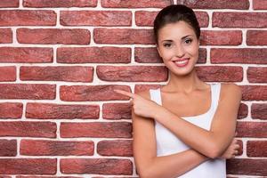 Beauty pointing copy space. Portrait of beautiful young short hair woman pointing away smiling while standing against brick wall photo