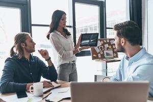 inspirado para trabajar duro. mujer joven moderna que señala el espacio de copia en la tableta digital mientras realiza una presentación de negocios en la oficina foto