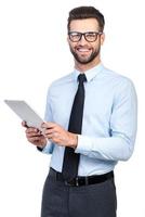 How may I help you Confident young handsome man in shirt and tie holding digital tablet and looking at camera with smile while standing against white background photo