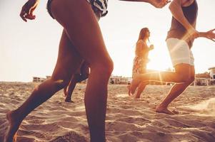 Unstoppable. Group of young cheerful people running along the beach and looking happy photo