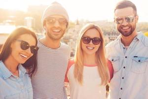 The best friends ever. Four young cheerful people bonding to each other and smiling while standing close to each other with great cityscape in the background photo