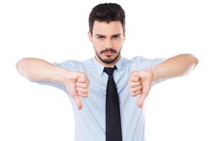 Rejected Confident young man in shirt and tie looking at camera and showing his thumbs down while standing against white background photo