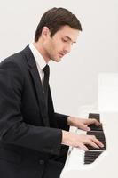 Music is everything. Confident young man in formalwear playing piano photo