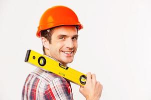 Cheerful construction worker. Rear view of handsome young handyman with carrying work tool on shoulder and looking over shoulder while standing against grey background photo