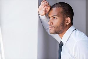 Looking for inspiration. Handsome young man in shirt and tie leaning at the wall and looking away photo