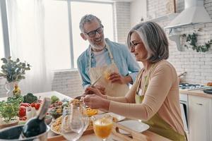 Positive senior couple in aprons preparing healthy dinner and smiling while spending time at home photo