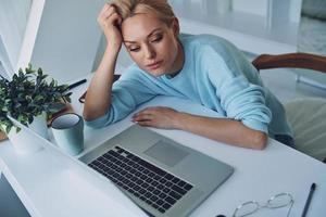 Top view of tired young woman using laptop while working in office photo